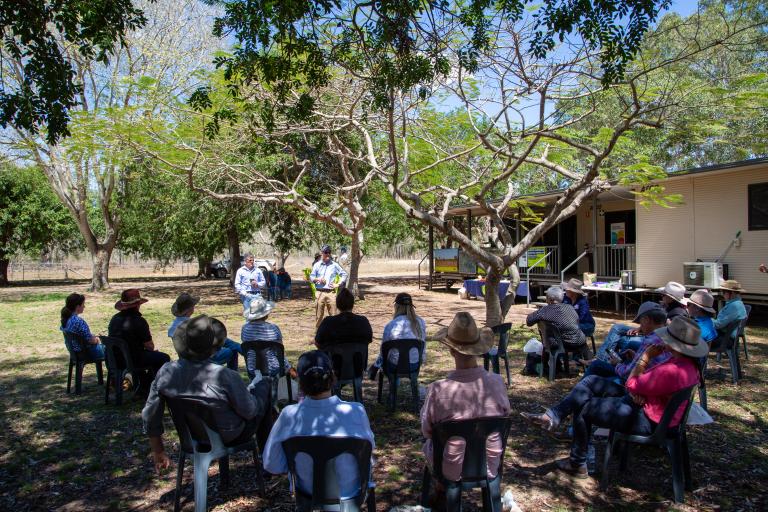 A photograph of a group of people sitting and listening to two speakers at a cattle research station.