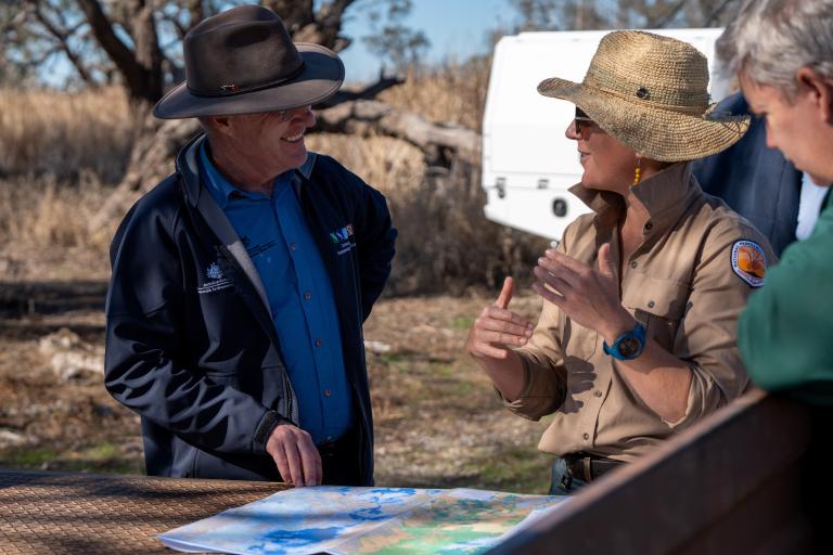 A photograph of 3 people having a conversation around a map.