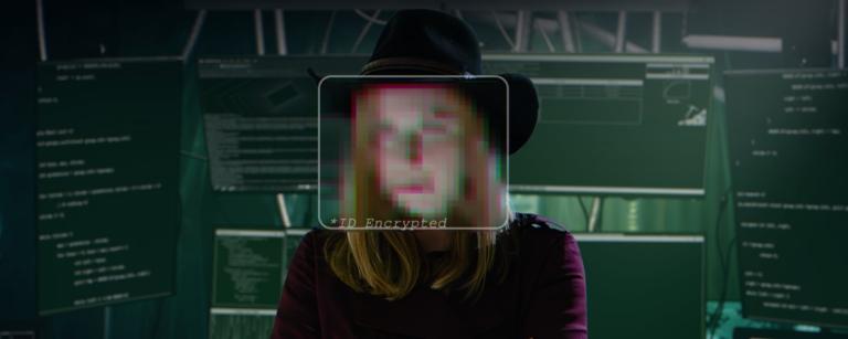 Person with an obscured face sitting in front of computer monitors displaying code and the text "id encrypted".