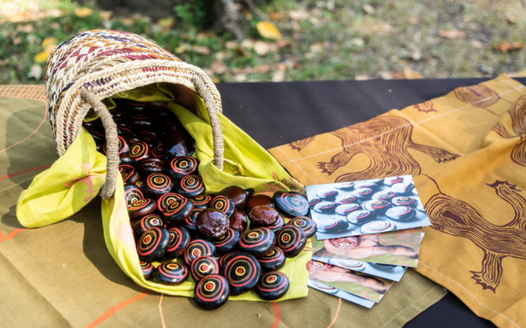 Basket of colourful painted Jawun Burnie Beans spilled onto a table next to a few scattered cards.