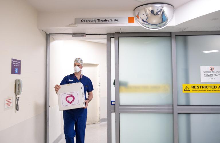 Hospital worker walking out of Operating Theatre Suite carrying a DonateLife organ transplant box.