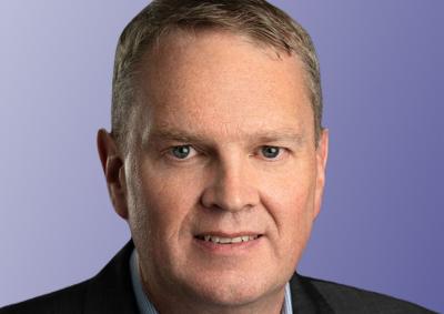 Portrait photo of a male presenting person in a collared shirt and jacket standing in front of a purple background