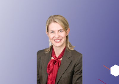 A photo of a professionally dressed woman on an abstract background that fades from white to deep purple horizontally. On the right side are abstract hexagons of different colours