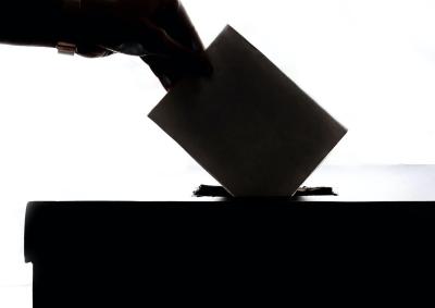 A silhouette image of a person putting a ballot in a ballot box