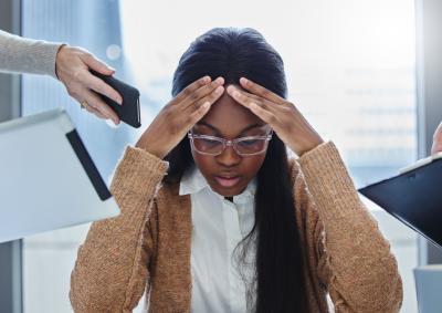 A man sits at his desk with his head in his hands, it is clear he is under pressure