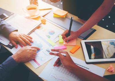 Image of three people's hands working together with post it notes, sheets of paper and an ipad 