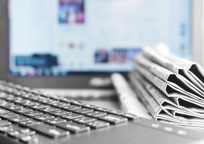 Image of a computer keyboard, a pile of newspapers and a blurred computer screen.