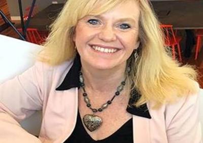 Image of Susan Horvath in a pink jacket with her right arm leaning against a desk. 