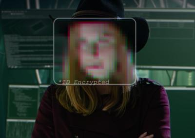 Person with an obscured face sitting in front of computer monitors.