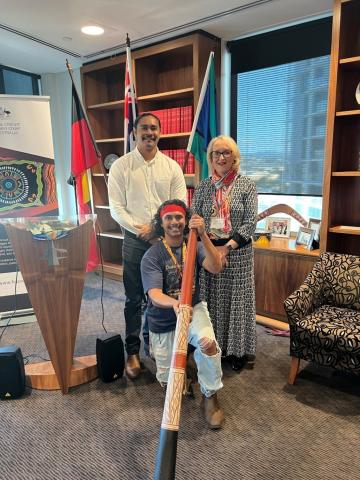 Indigenous Family Liaison Officer Frank Watson-Brown, Judge Willis of the FCFCOA (Division 2), Chair of the Courts’ Access to Justice Committee and local cultural performer Jahmarley Dawson holding a didgeridoo smiling at the camera. 