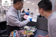 A border control officer engaging with a passenger who has items out for inspection on a table